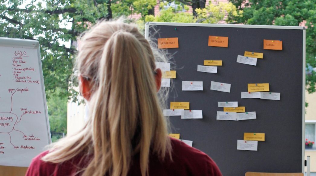 A young woman looks at blackboards and a whiteboard with labeled slips of paper. 