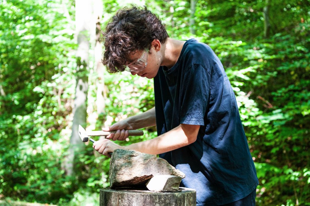 A teenage volunteer works on memorial stones of the Buchenwald Railway Memorial Trail with a hammer and chisel.