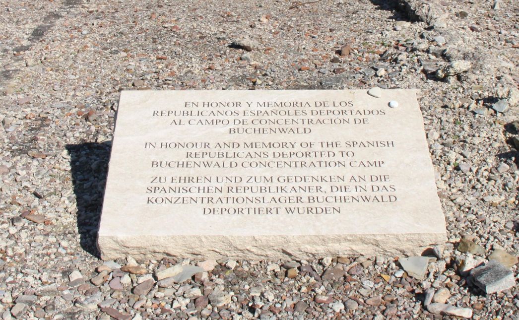 Weißer Gedenkstein mit dem Schriftzug Schriftzug: "Zu Ehren und zu Gedenken an die spanischen Republikaner, die in das Konzentrationslager Buchenwald deportiert wurden“ Auf spanisch, englisch und deutsch. 