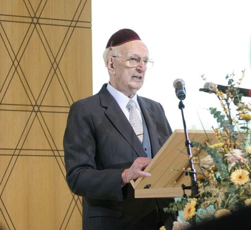 Alfred Salomon bei der Einweihung der neuen Synagoge in Bochum. Er steht an einem mit Blumen verzierten Rednerpult mit Mikrofon. Er trägt einen schwarzen Anzug und eine schwarze Kippa.