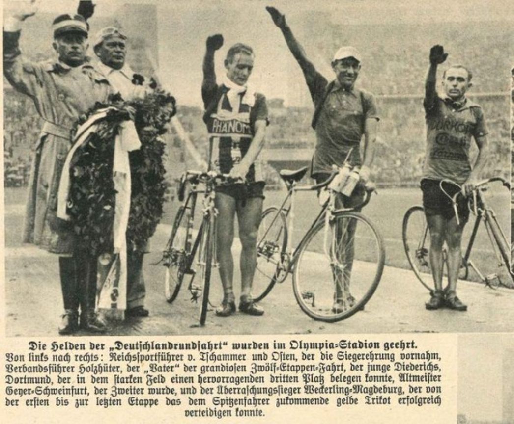 Newspaper clipping with a black and white photograph. Three cyclists at a victory ceremony with their arms raised in the Hitler salute. To the left of them is the Reichsportführer Hans von Tschammer and Osten.