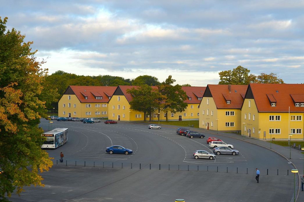 Ein Parkplatz mit 4 länglichen Gebäuden. Der Parkplatz hat eine halbrunde Form.