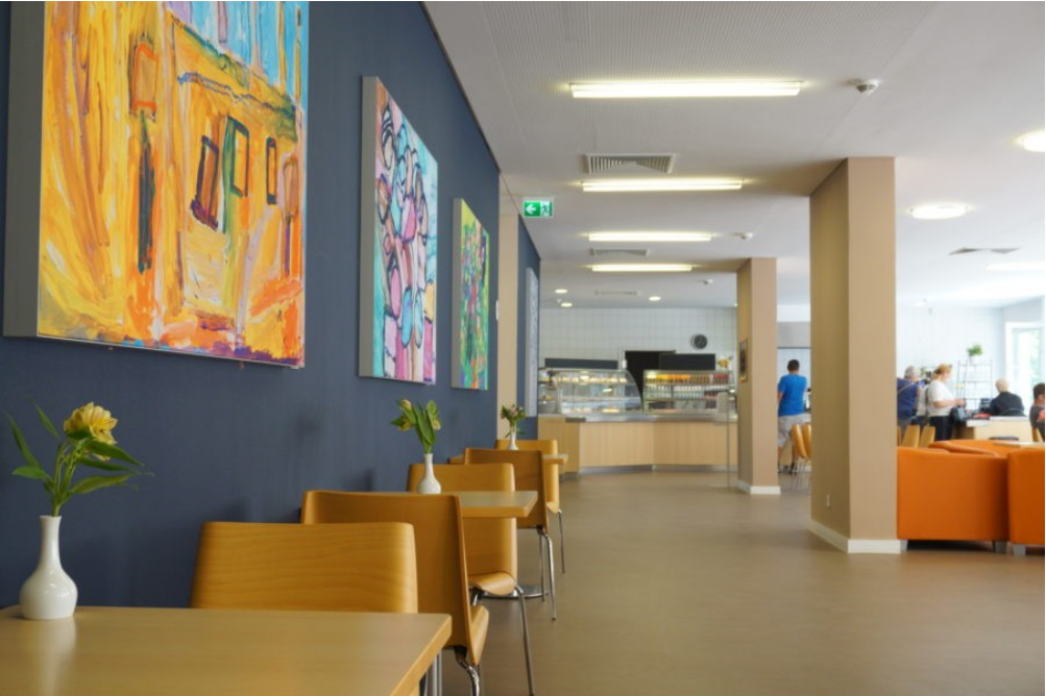 Das Café Paul von innen: Tische und Stühle aus Holz stehen entlang der Wand. An der Wand hängen farbige Gemälde.
