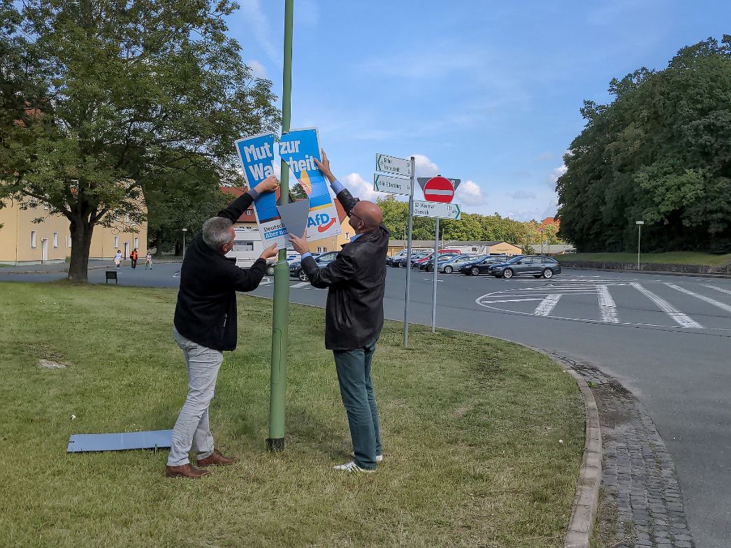 Das Foto zeigt zwei Männer beim Abnehmen eines AfD Plakates mit dem Slogan „Mut zur Wahrheit“.