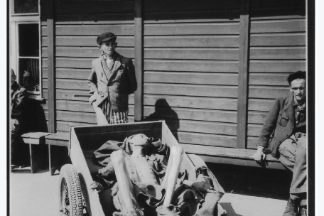 An extremely emaciated prisoner lies weakened in a cart in the liberated camp. Behind him, other prisoners.