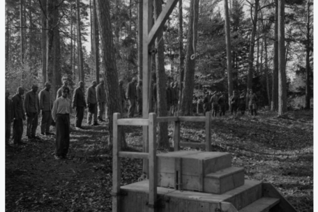 Prisoners stand behind a gallows.
