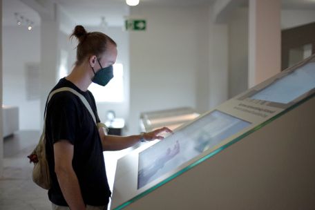 A young man stands in front of a touchscreen in the exhibition.