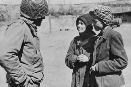 Two women are talking with an American soldier in uniform and helmet. 