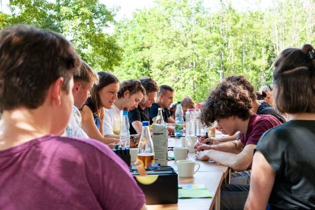 Eine Gruppe junger Menschen arbeitet an einem Tisch im Freien. 