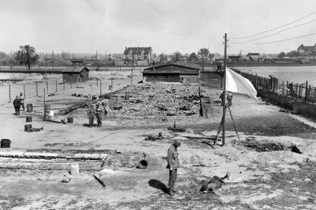 The photo shows the remains of a barrack. Beside the ashes lie scattered burned corpses.