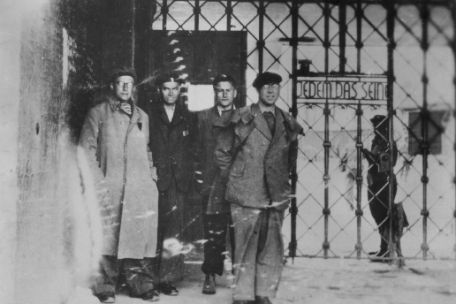 Hermann Brill and three other men stand in front of the camp gate inscription "To each his own", which is attached to the inside. 