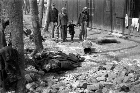 Two prisoners lead an infant by the hands past Barrack 66 while another prisoner walks behind them. They look down intently at the child. In the foreground of the picture, a dead prisoner lies on a pile of rubble. He is wrapped in a blanket, but the face is recognizable. Clothes are hanging out of the window of the barracks. 