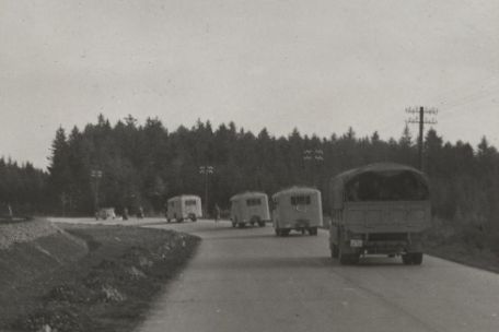 Angehörige der SS-Kraftfahr-Ausbildungs und-Ersatz-Abteilung fahren mit Lastwagen und Bussen auf der Blutstraße zur Vereidigung nach Weimar. Dazwischen einige Motorräder. Neben der Straße verläuft eine Stromleitung. 