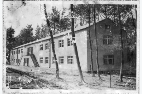 Elongated two-story building surrounded by trees.