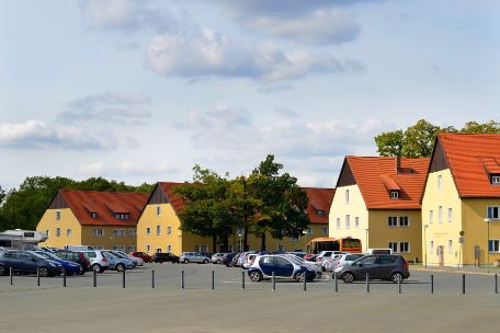 Blick auf den Parkplatz der Gedenkstätte. Daneben die ehemaligen SS-Kasernengebäude, die heute durch die Gedenkstätte genutzt werden. 