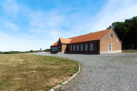 View of the single-story building that was formerly the prisoners' canteen. The two identical wings of the building are separated in the middle by an entrance area with a pointed roof.