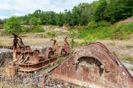 A rusty tipper truck and its rusty rail undercarriage. In the background partly bare, partly overgrown steep slopes.