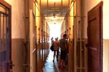 View into the cross corridor of the detention cell building. Individual visitors stand in front of various cells and look inside.