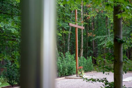 Im Vordergrund des Bildes eine der Stahlstelen. Dahinter das hölzerne Kreuz. Vor dem Kreuz wurden Gedenkkerzen abgelegt.