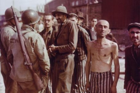 Emaciated liberated prisoners of the Little Camp talking to American soldiers. An emaciated shirtless former prisoner looks directly into the camera.