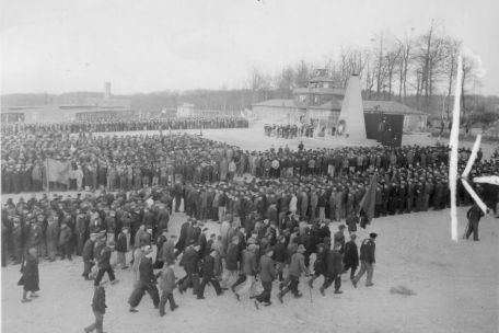 Befreite Häftlinge bei der ersten Gedenkfeier für die Toten des KZ Buchenwald. Im Hintergrund ist das provisorische Mahnmal für die Toten zu sehen.