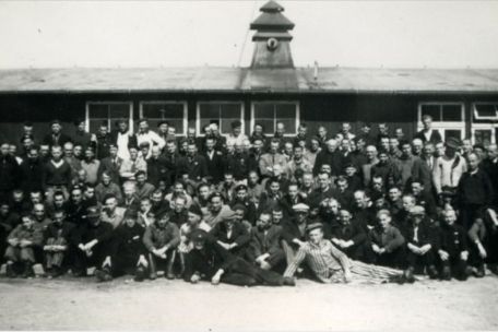 Gruppenfoto befreiter niederländischer Häftlinge vor einer Holzbaracke. Vereinzelt tragen einige noch immer Häftlingskleidung.