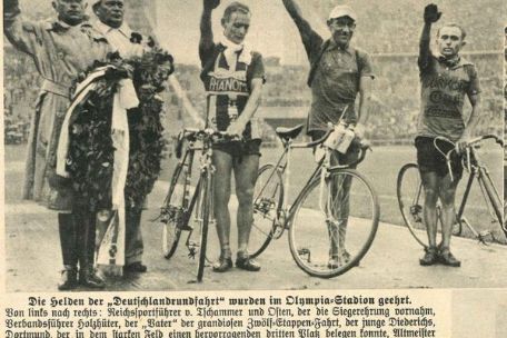Zeitungsausschnitt mit einer Schwarzweißfotografie. Drei Radfahrer bei einer Siegerehrung, die ihren Arm zum Hitlergruß erhoben haben. Links neben Ihnen steht der Reichsportführer Hans von Tschammer und Osten.