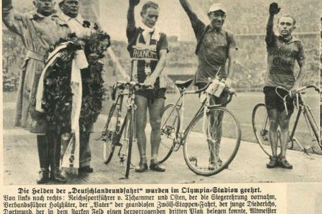 Newspaper clipping with a black and white photograph. Three cyclists at a victory ceremony with their arms raised in the Hitler salute. To the left of them is the Reichsportführer Hans von Tschammer and Osten.