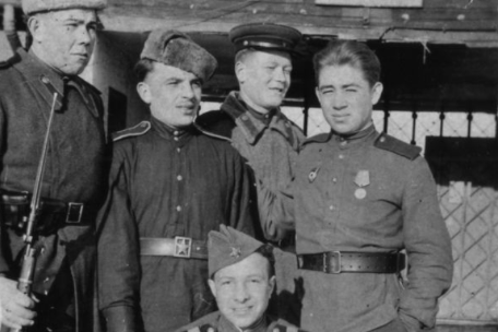 Five Soviet soldiers. Four are standing in front of the camp gate of the recently established Special Camp No. 2, one is kneeling in the foreground. All of them are looking at the camera.