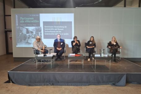 Fünf Menschen sitzen vor einer Leinwand auf einem Podium.