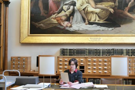 Shot of Constance Py-Fauvet sitting at a workstation. Spread out in front of her are some papers.