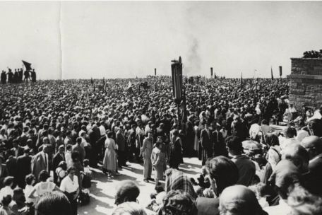 A large crowd has gathered between the bell tower and Fritz Cremer's group of figures.