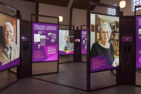 Exhibition view featuring large portrait photographs and informational panels with text