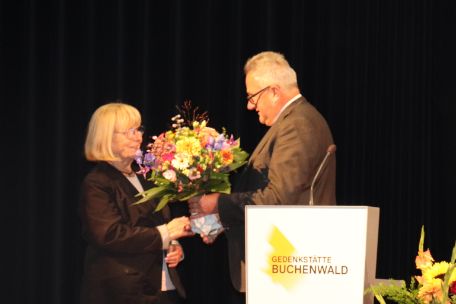 Der Direktor der Gedenkstätte Buchenwald Jens-Christian Wagner überreicht Heidrun Brauer am Rednerpult einen großen Blumenstrauß zum Dank für ihren Einsatz für die Speziallager-Erinnerung.