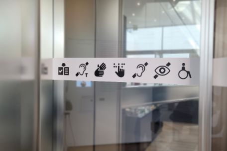 Auf einer Glastür ist in Form von Symbolen angezeigt, welche inklusiven Zugänge alle in der Ausstellung verwirklicht wurden.