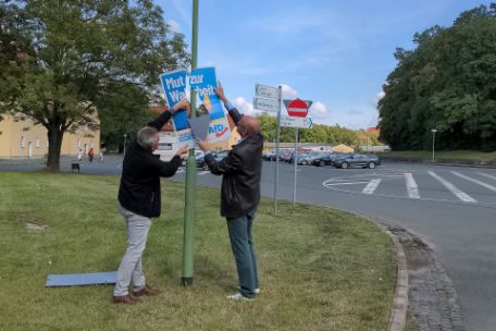 Das Foto zeigt zwei Männer beim Abnehmen eines AfD Plakates mit dem Slogan „Mut zur Wahrheit“.