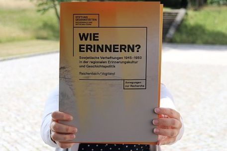 Eine Person hält eine Mappe vor die Kamera. Sie trägt den Titel "Wie erinnern?"