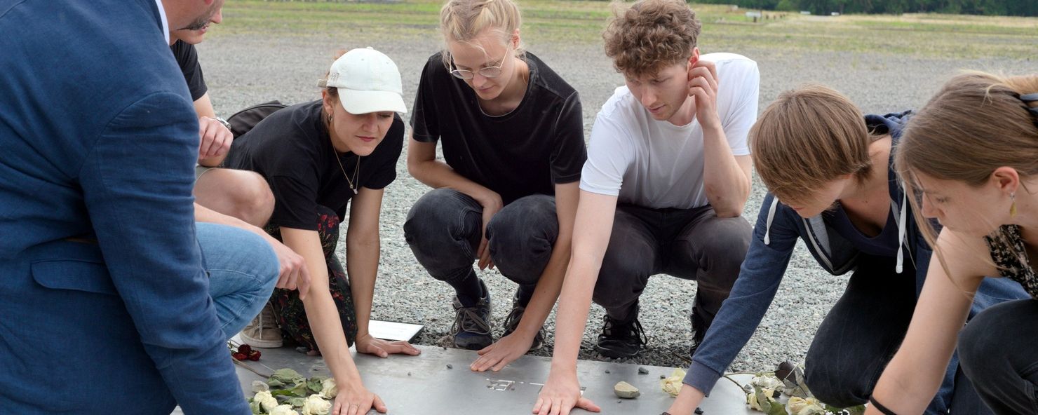 A group of young visitors with their guide touching the memorial plaque at Appellplatz.