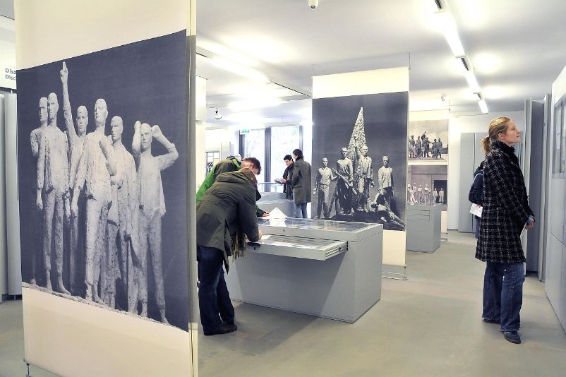 The photo shows people in the exhibition building reading information boards and examining display cases.
