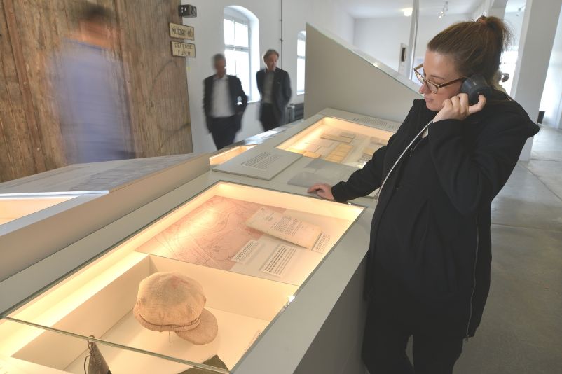 A visitor stands in front of a display case and listens at a listening station.