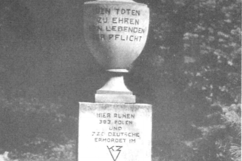 Eine steinerne Urne steht auf einem Steinblock. Die Urne trägt die Aufschrift "Den Toten zu Ehren, den Lebenden zur Pflicht". Der Stein erinnert an ermordete Polen und Deutsche im KZ Sachsenhausen. 