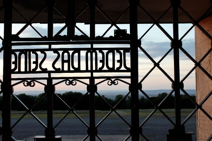View through the camp gate onto the prisoners' compound at dusk. The slogan Jedem Das Seine in the camp gate can be seen from behind.