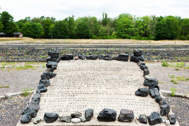 Grauweißer Gedenkstein mit der Gravur:" Block 1, 7, 13, 19, 25, 30. Lager Sowjetischer Kriegsgefangener. Allem Völkerrecht zum Hohn wurden sowjetische Soldaten in Buchenwald gefangen gehalten. Neben schwerster Arbeit wurden sie grausam gequält und viele starben trotz solidarischer Hilfe durch die politischen Gefangenen an Erschöpfung und Hunger." in Deutsch, Russisch und Französisch.