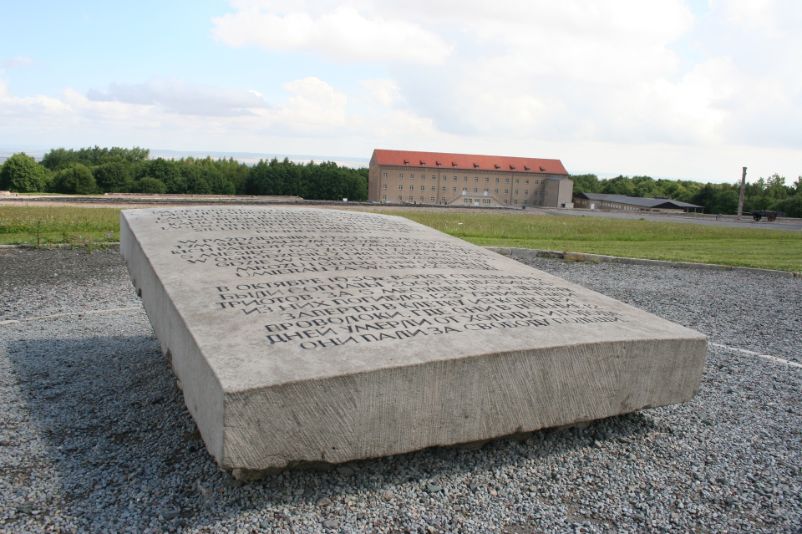 Grauer Gedenkstein mit der Aufschrift: "Im Oktober 1939 kamen 2098 polnische Patrioten in dieses Sonderlager. 1650 starben in 5 Monaten. 123 wurden in einen Stacheldrahtkäfig gesperrt, in dem sie nach 12 Tagen erfroren und verhungerten. Sie litten und starben für die Freiheit Polens." in, Deutsch, Polnisch, und Russisch.