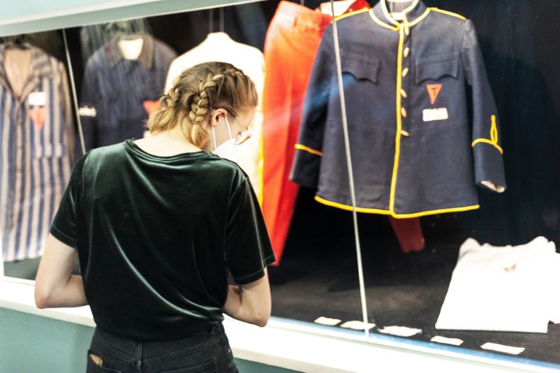 A young woman looks at a glass cabinet displaying prisoners' clothing.