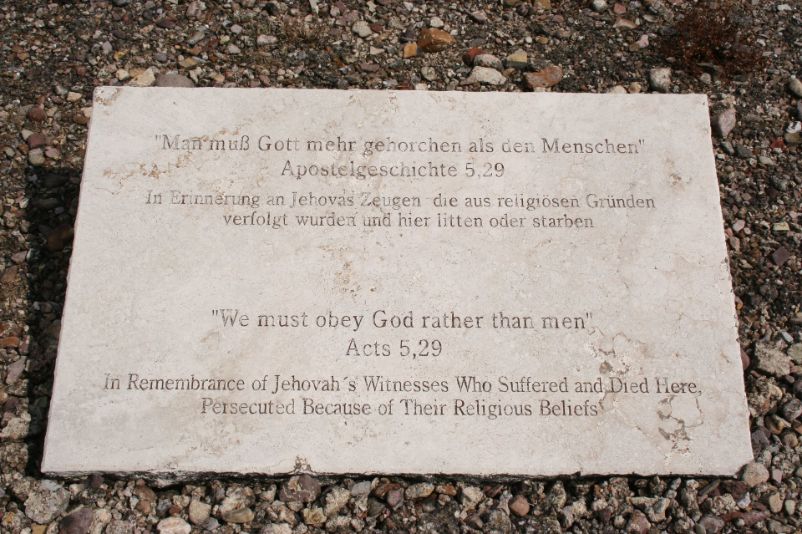 White memorial stone engraved, "We must obey God rather than men Acts 5:29. In memory of Jehovah's Witnesses who were persecuted for religious reasons and suffered or died here." In English and German.