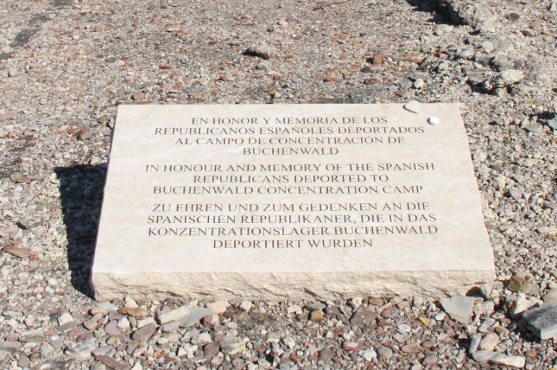 Weißer Gedenkstein mit dem Schriftzug Schriftzug: "Zu Ehren und zu Gedenken an die spanischen Republikaner, die in das Konzentrationslager Buchenwald deportiert wurden“ Auf spanisch, englisch und deutsch. 