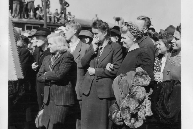 Eine Nahaufnahme zahlreicher Weimarer Bürger:innen im befreiten Lager. Mittig im Foto steht eine Frau und hält sich ein Taschentuch an die Nase.