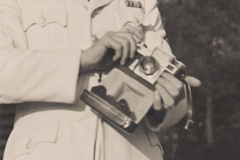 Ausschnitt aus einem Foto. Lagerkommandant Karl Koch mit einem Fotoapparat vor seinem Haus in der SS-Führersiedlung. Nur seine Hände und die Kamera sind sichtbar.