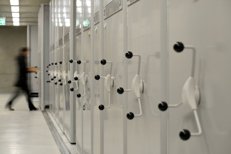 Close-up of the rolling racks. In the deep storage magazine in the background, an employee pushes a file cart.